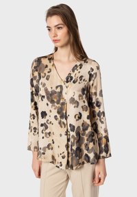 Blusa in stampa leopardata beige, con scollatura a V, maniche lunghe e tessuto leggero e morbido con un design fluido. Taglio semplice e moderno.