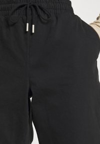 Czarne spodnie o luźnym kroju, wykonane z miękkiego materiału, z elastycznym paskiem w talii i sznurkiem do regulacji, oraz skośnymi kieszeniami po bokach.