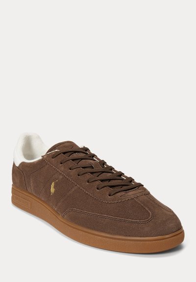Καφέ σουέτ sneaker χαμηλού τύπου με καφέ κορδόνια, λαστιχένια σόλα, λευκή εσωτερική επένδυση και μικρό χρυσό λογότυπο στη πλευρά.