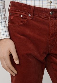 Rote Cordhosen zeichnen sich durch eine schmale Passform, eine vertikale Rippstruktur, ein Fünf-Taschen-Design und einen kleinen dekorativen Stich an der vorderen Tasche aus.
