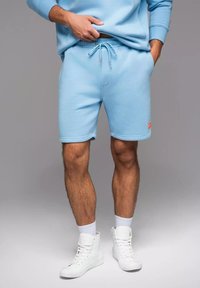 Lichtblauwe katoenen shorts in een mix met elastische tailleband en koordje. Bevat zijzakken en een oranje logo op de onderrand.