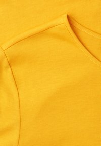 Gros plan sur un tissu jaune vif montrant une couture cousue et le bord du col d'un vêtement en maille douce, probablement un t-shirt ou un pull.