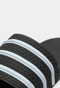 Sandale noire en caoutchouc à glissière, dotée de trois bandes noires texturées avec des accents bleu clair. La semelle intérieure est lisse et la semelle extérieure est mate.