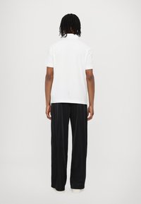 White cotton polo shirt with short sleeves, paired with black wide-leg trousers. The outfit features a relaxed fit and minimal detailing.