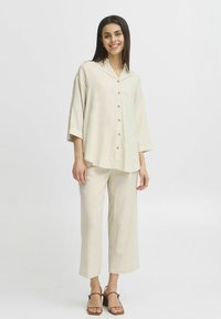 Camicia di lino beige con colletto e bottoni, abbinata a pantaloni cropped larghi coordinati. Sandali piatti marroni.
