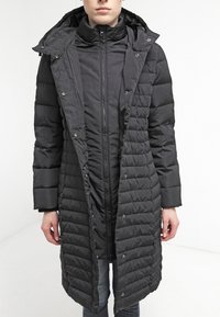 Black padded coat with a long silhouette, zippered front, snap buttons, and a hood. Features quilted texture and side pockets.
