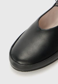 Pantofii din piele neagră, cu vârf rotunjit, textură netedă și un profil joasă, având un design minimalist și fără hardware vizibil.