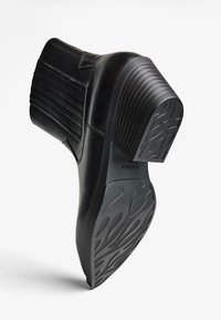 Črne usnjene gležnjarje z rebrastim detajlom, debelim petnim delom in teksturirano gumijasto podplatom z edinstvenim vzorcem za oprijem.