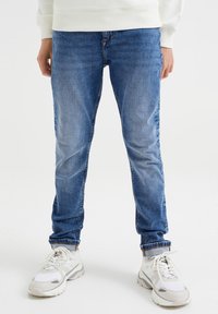Jeans de denim azul claro con un corte ajustado, textura desgastada y un sutil efecto de arrugas. Cuenta con un diseño clásico de cinco bolsillos y puños enrollados.