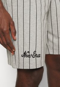 Grå bomullsshorts med svarta vertikala ränder och broderad "New Era"-logotyp. Har sidofickor och ett elastiskt midjeband.