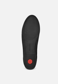 Schwarze Gummisohle mit strukturierten Oberflächen, die ein achteckiges rotes Akzent und Branding aufweist. Glatte Kanten mit flachem Profil.