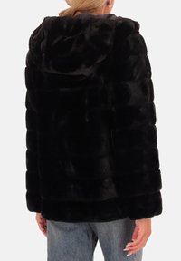 Zwarte nepbontjas met een capuchon, doorgestikt ontwerp en een relaxte pasvorm. Zachte textuur met opvallende stiksels op de rug.