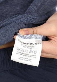 Tummansininen vaatteiden etiketti, jossa on hoito-ohjeet ja kankaan koostumus: 60% merinovillaa, 40% tenceliä, pehmeällä ja sileällä pinnalla.