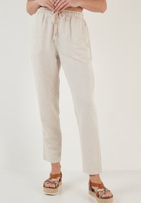 Lichtbeige tapse broeken met een elastische tailleband en trekkoord. Gestyleerd met bruine strapsandalen met een plateauzool, die een gestructureerde stof tonen.