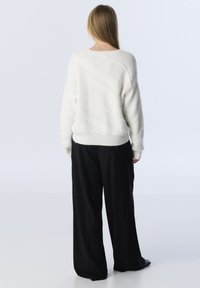Pull en tricot blanc avec des détails de texture diagonale, associé à un pantalon noir ample. La vue de dos révèle une coupe décontractée et des bords côtelés.