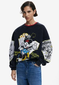 Tamsiai mėlynas džemperis su Mickey Mouse grafika, apipinta gėlėmis, geltonais užrašais ir raštuotomis rankovėmis. Ripsinė apykaklė ir rankogaliai.