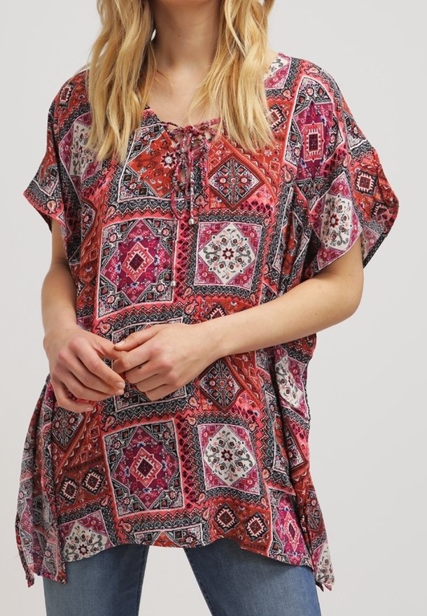 Tunique à manches courtes et ample en rose et rouge vifs, présentant un motif de patchwork géométrique avec des accents floraux et un détail à nouer au niveau du col.
