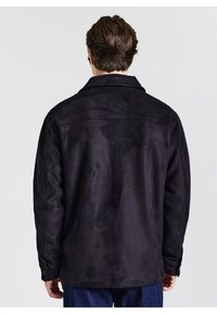 Schwarze Wildlederjacke mit lockerer Passform, großem Kragen und geknöpften Manschetten, die eine glatte Textur und ein minimalistisches Design zeigt.