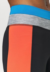 Legginsy sportowe z wysokim stanem, z kolorowym wzorem w blokach w odcieniach niebieskiego, szarości, pomarańczy i czerni; gładka tekstura i elastyczny pas.