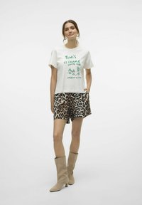 Witte t-shirt met groene grafische tekst "Toni's Ice Cream & Sundae Club," gecombineerd met leopardprint shorts en lichtbruine kniehoge laarzen.