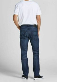 Mörkblå slim-fit jeans i denim, med bakfickor och en läderpatch i midjan, matchade med en vit t-shirt och svarta sneakers.