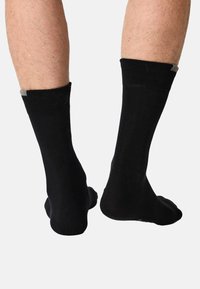 Sorte bomuldssokker med en glat tekstur, midt på læggen længde og en grå detalje øverst. Enkelt design uden mønstre eller yderligere funktioner.