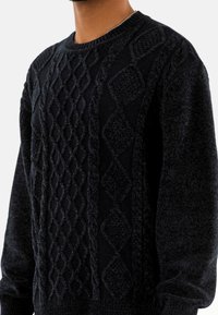Maglione nero a maglia con motivi a cavo e a diamante, collo a giro e polsini a costine. Realizzato in un morbido filato spesso.