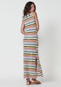 Gestreiftes Maxikleid aus mehrfarbigem Garn, mit enganpassendem Design, hohem Hals und seitlichem Schlitz. Kombiniert mit braunen Riemchensandalen.