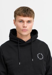 Felpa nera con cappuccio realizzata in misto cotone, dotata di tasca frontale, cappuccio con cordino e logo circolare bianco sul lato sinistro del petto.