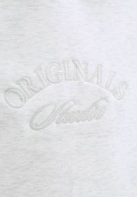 Sudadera de color gris claro con tejido texturizado. Presenta "ORIGINALS" y "Studio" bordados en gris claro en la parte frontal.