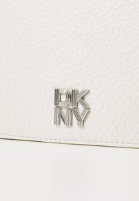 Bolso de cuero texturizado blanco con un logotipo plateado de DKNY. La superficie está estampada con un fino patrón, lo que proporciona un interés visual sutil.