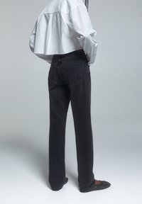 Mörkgrå jeans med rak benstil, med bakfickor och diskret sömnad. Bärs med en kortärmad vit skjorta. Slät textur.