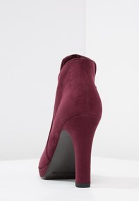 Burgundy korkokenkä nilkkuri, jossa on sileä mokka viimeistely, pyöreä varvas ja kiinte�ä musta pohja, jossa on pieni alusta edessä.