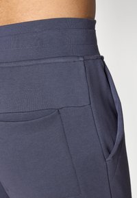 Námornícky modré športové šortky s širokým elastickým pásom, bočnými vreckami a hladkým, textúrovaným materiálom.