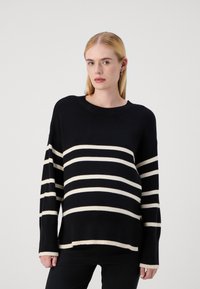 Črno-bela stripe pulover z širokim rebrastim ovratnikom in dolgimi rokavi. Stripe so enakomerno razporejene, material pa se zdi mehak.