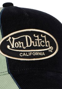 Black corduroy cap featuring a beige oval patch with "Von Dutch" and "CALIFORNIA" in black lettering. Includes contrasting green side panels.