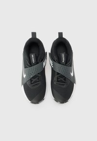 Čierne športové topánky s priedušným zvrškom, textúrovaným šedým pásom, bielym logom Nike a čiernymi šnúrkami. Obsahujú polstrovaný jazyk a pútko na päte.