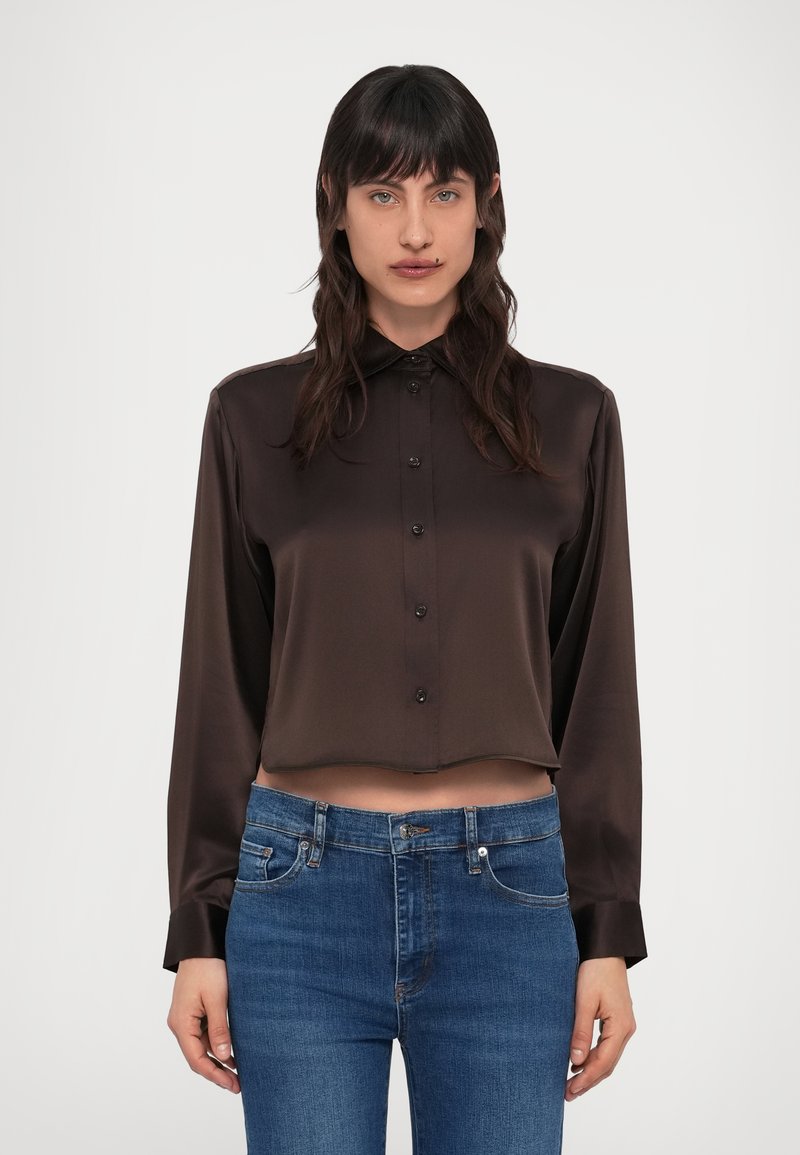 Hnedá saténová košeľa na zapínanie s orezaným lemom, dlhými rukávmi a klasickým golierom, doplnená svetlomodrými džínsami.