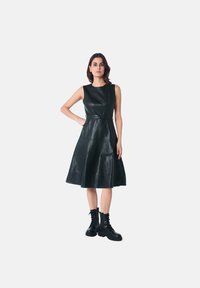 Robe noire en cuir de style A, sans manches, avec une taille cintrée et une jupe évasée. Présente une texture lisse et un détail de boutons.