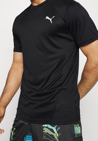 Camiseta deportiva negra hecha de tejido transpirable, con un logo blanco de Puma en el pecho y un panel de malla texturizada en el costado.