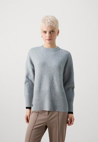 Hellgrauer Wollpullover mit geripptem Saum und Bündchen, runder Ausschnitt und lockerer Passform, kombiniert mit beigen, taillierten Hosen.