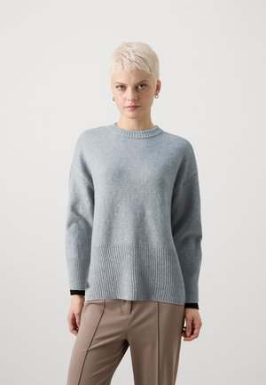Vaaleanharmaa villapaita, jossa on ribbireunat ja hihat, pyöreä pääntie ja löysä istuvuus. Yhdistetty beigen värisiin siisteihin housuihin.
