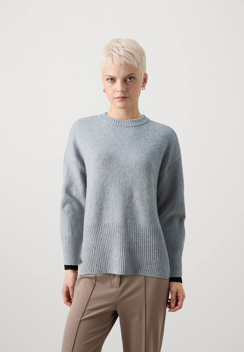 Hellgrauer Wollpullover mit geripptem Saum und Bündchen, runder Ausschnitt und lockerer Passform, kombiniert mit beigen, taillierten Hosen.