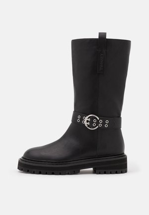 Botte noire mi-mollet avec semelle épaisse, boucle ronde argentée et détail de ceinture à œillets, avec languette marquée en haut.
