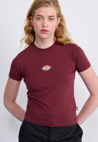 Bordo majica kratkih rukava s prilagođenim dizajnom, s kružnim logotipom u plavoj, žutoj i crvenoj boji na prsima. Mekani pamučni materijal.