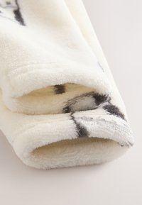 Tissu polaire doux de couleur crème avec des motifs abstraits noirs ; présente une texture lisse et des bords arrondis, idéal pour la chaleur et le confort.