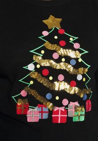 Pull noir avec un sapin de Noël brodé, une étoile dorée, des ornements colorés et des boîtes cadeaux de différentes couleurs à la base.