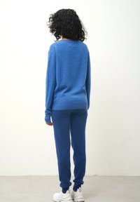 Blå stickad tröja och matchande joggers, båda tillverkade av mjukt, texturerat tyg, med ribbade muddar och en avslappnad passform. Vita sneakers fulländar looken.