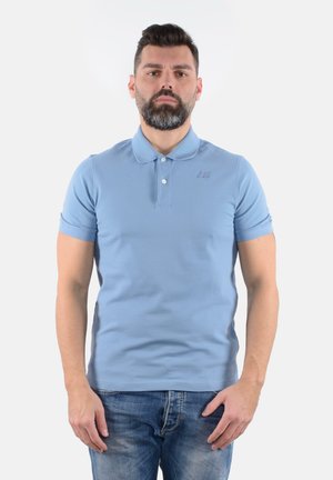 Polo azzurro chiaro con maniche corte, tre bottoni e un logo strutturato sul petto. Abbinato a jeans in denim sbiaditi.