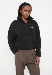 Czarny polarowy pulower z półzamkiem, posiadający kieszeń na piersi oraz logo North Face na lewym górnym boku. Fakturowana tkanina.